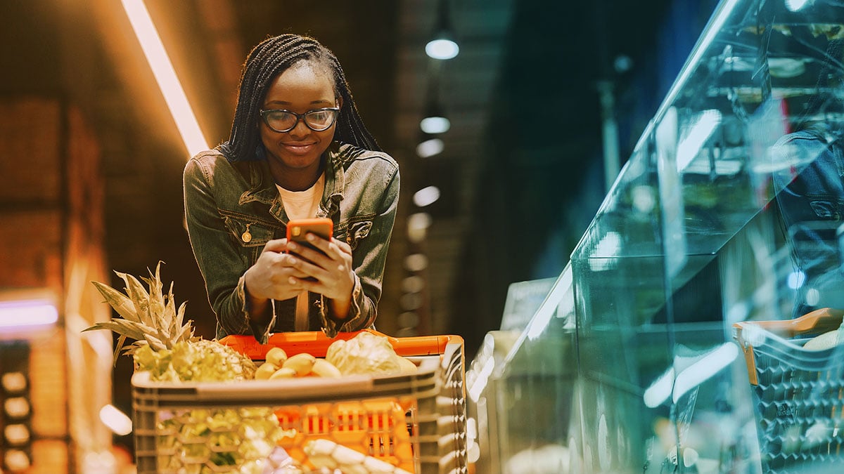 person grocery shopping pushing a cart and looking at list on phone